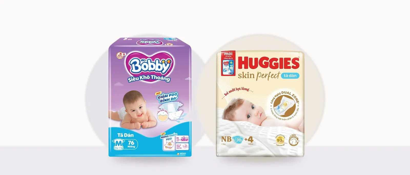 Bịch tã dán Bobby Siêu Khô Thoáng size M 76 miếng bao bì tím xanh đặt cạnh bịch tã dán Huggies Skin Perfect size NB 70+4 miếng bao bì màu kem