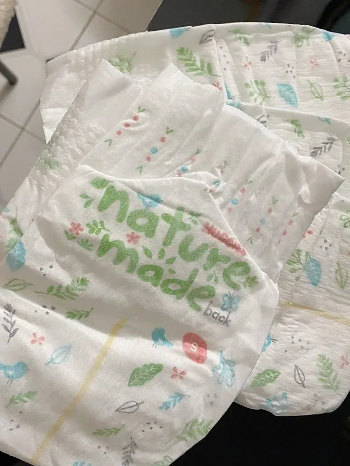 Mặt lưng miếng tã dán Huggies Nature Made in chữ nature made màu xanh lá, họa tiết lá cây và vạch báo tè màu vàng