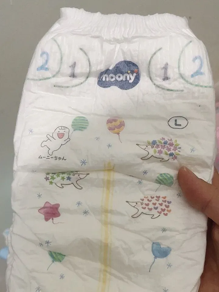 Tay cầm một miếng bỉm dán Moony size L in hình nhím và bóng bay, có vạch vàng dọc giữa