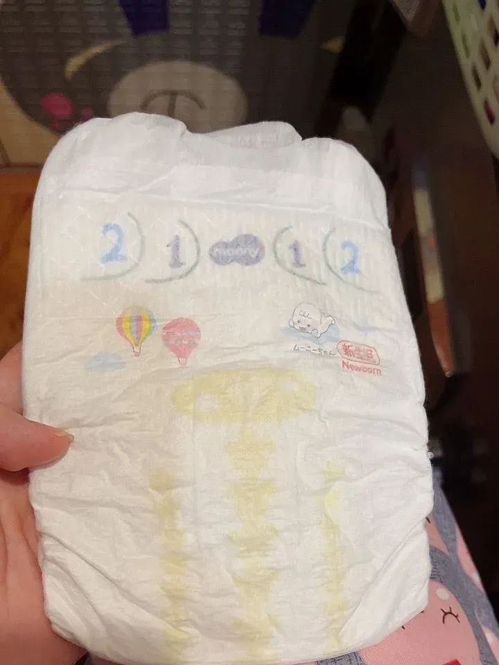 Tay cầm một miếng bỉm dán Moony size NB in hình khinh khí cầu và chữ Newborn